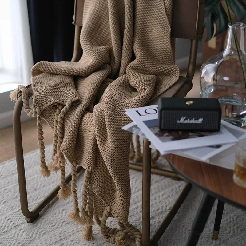 Beige knitted blanket draped over a chair with a Marshall speaker and magazine on a table in the background.