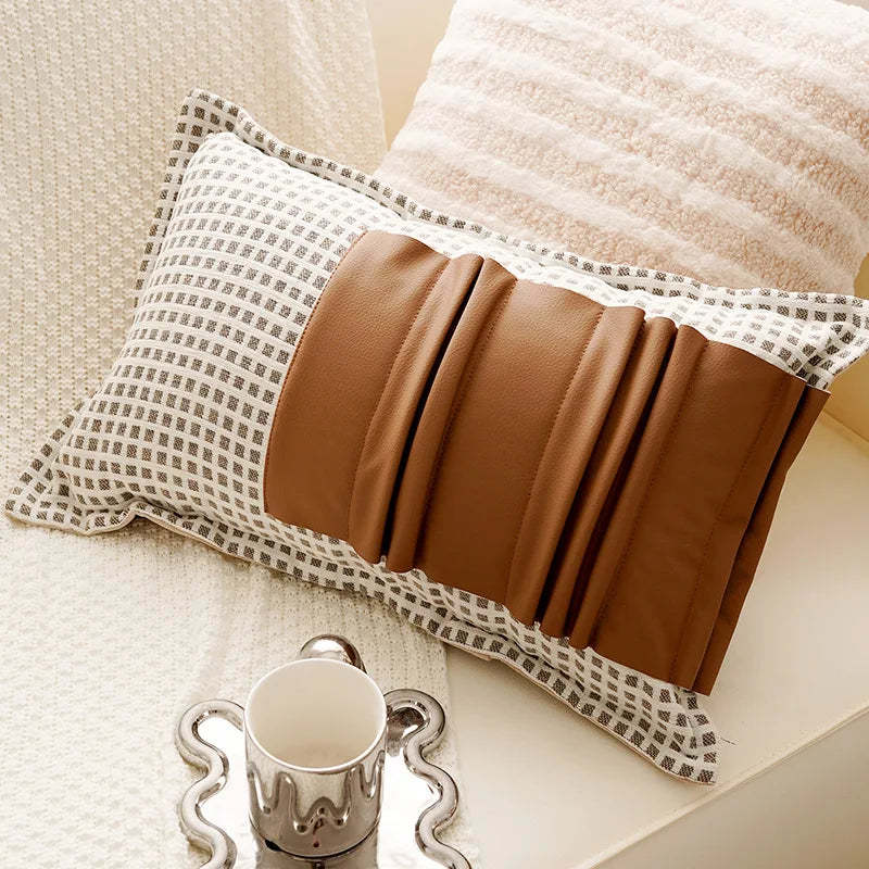 Decorative pillow with a brown accent on a beige surface next to a silver tray and white cup.