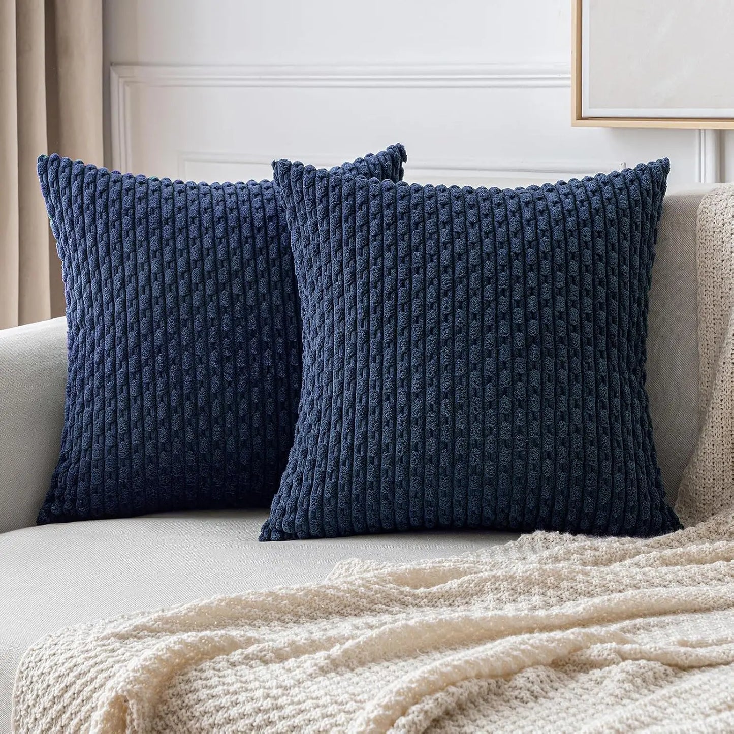 Two blue textured pillows on a beige sofa with a white wall in the background
