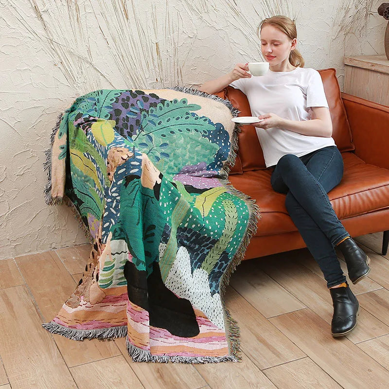 Woman sitting on a brown leather couch with a colorful patterned blanket draped over a chair. Boho Home Decor.