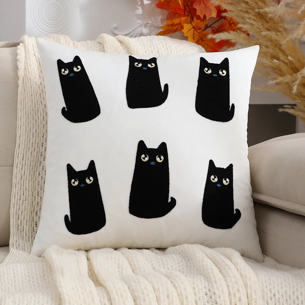 White pillow with black cat illustrations on a beige couch.