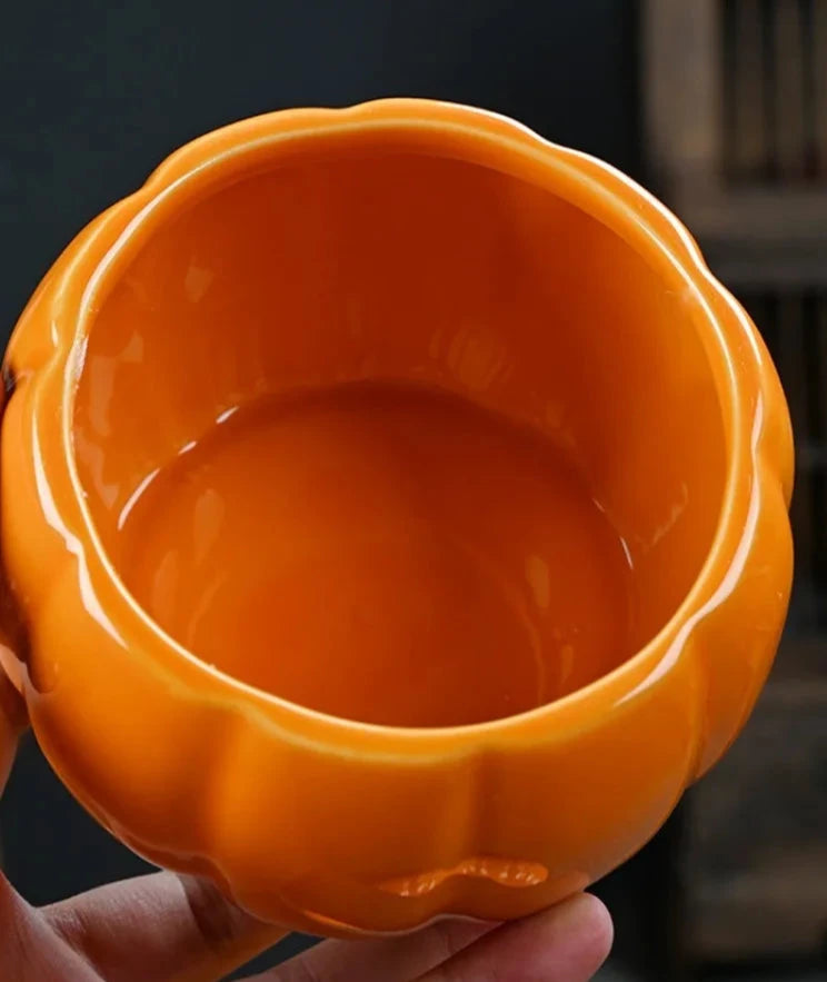 Orange ceramic pot held in a hand with a blurred background. Ceramic pumpkin candy jar with lid, decorative fall tea jar or wedding gift container for home or halloween holiday decor.