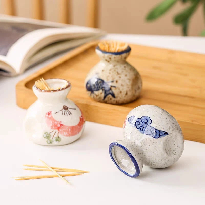 Three ceramic toothpick holders with decorative designs on a wooden tray.