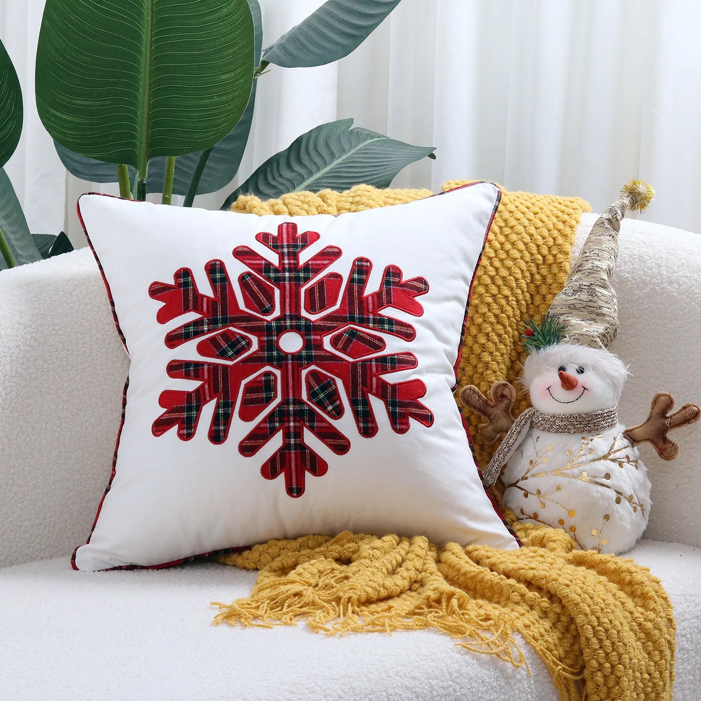 Decorative pillow with red snowflake design on a white couch with yellow blanket and snowman toy.