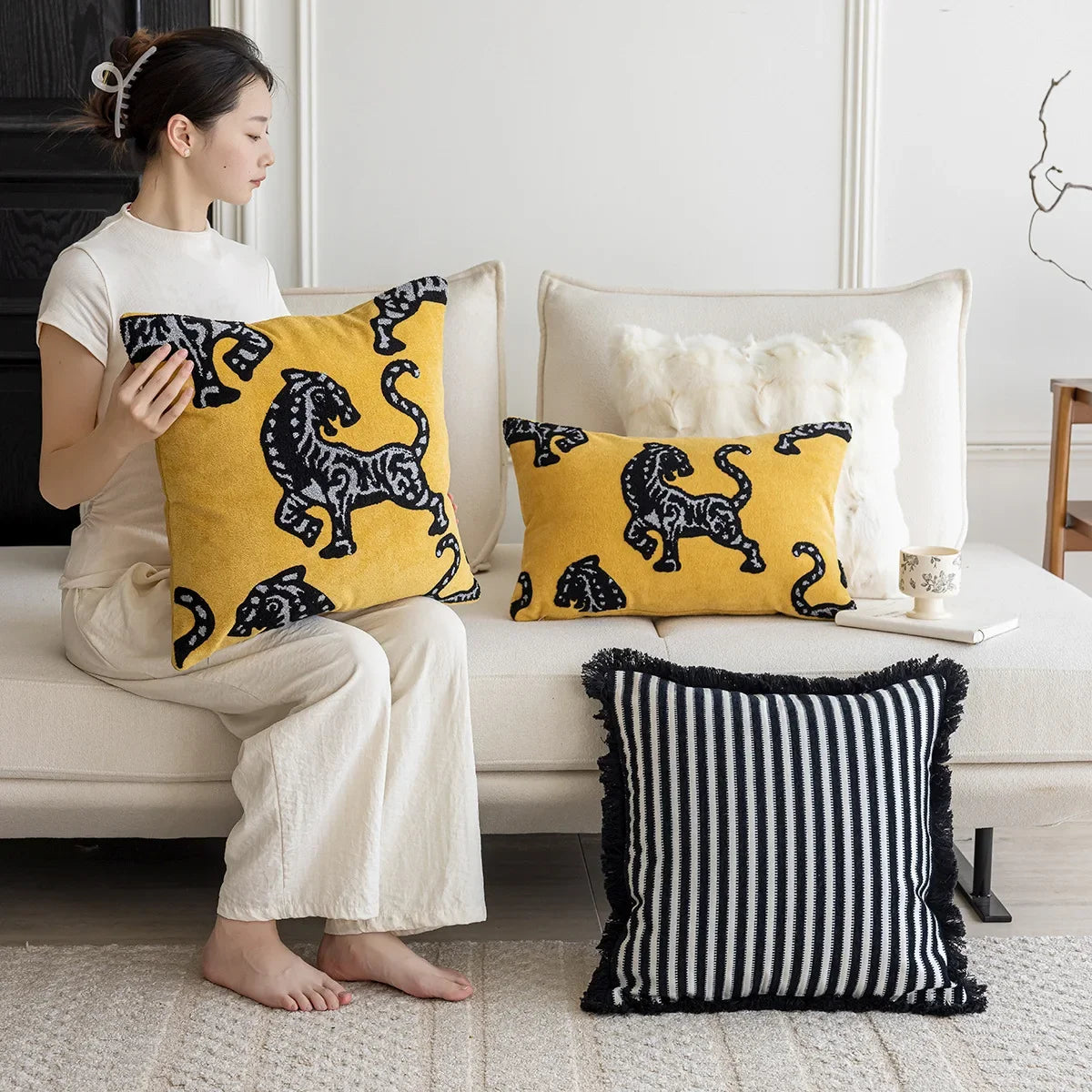 Woman holding a yellow pillow with black tiger design in a living room setting. Modern minimalist embroidered pillow cover for living room decor.