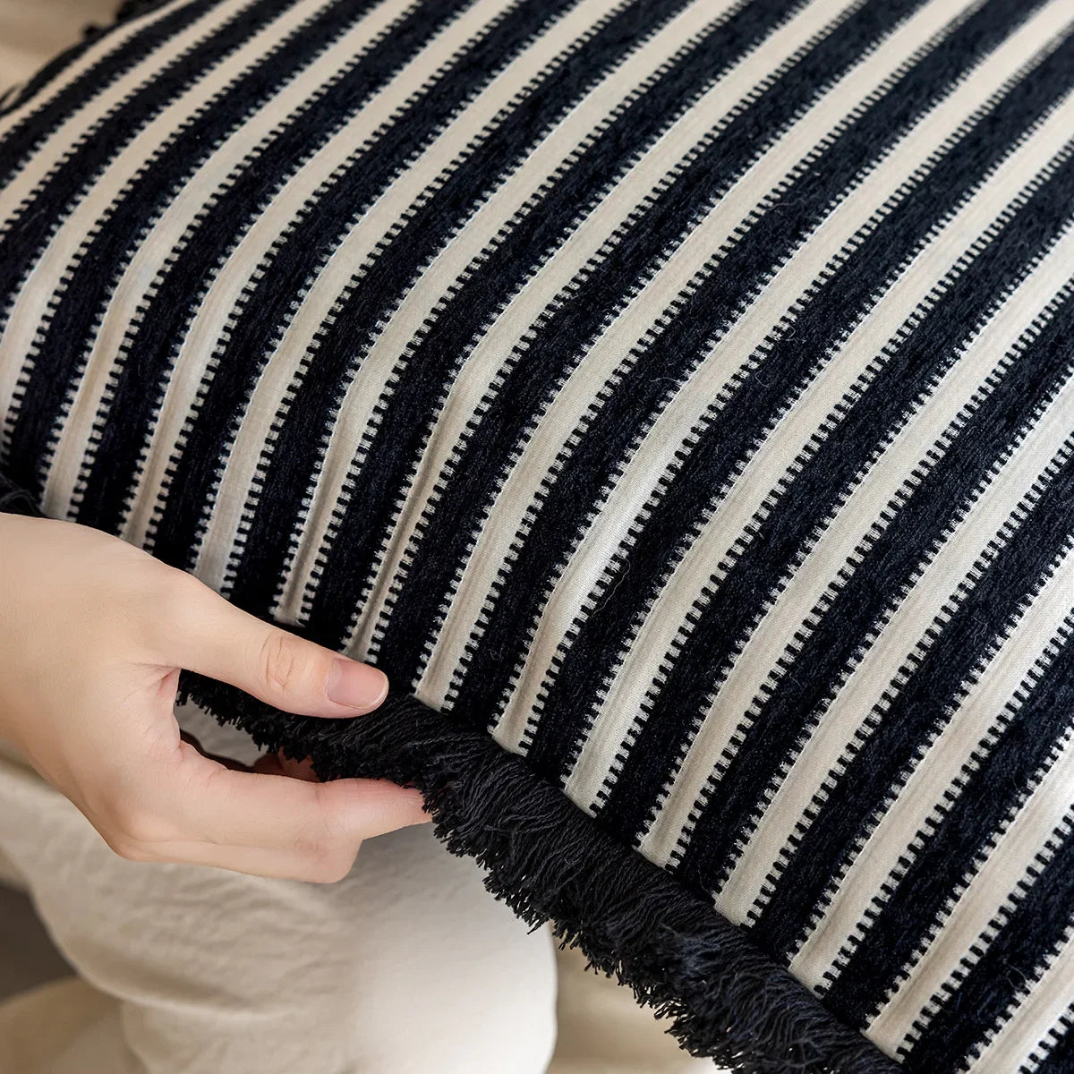 Black and white striped pillow with a hand touching it. Modern minimalist embroidered pillow cover for living room decor