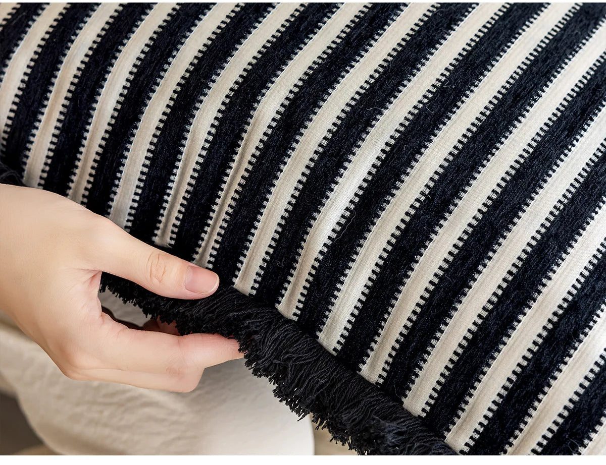 Close-up of a hand touching a black and white striped fabric with fringe. Modern minimalist embroidered pillow cover for living room decor.