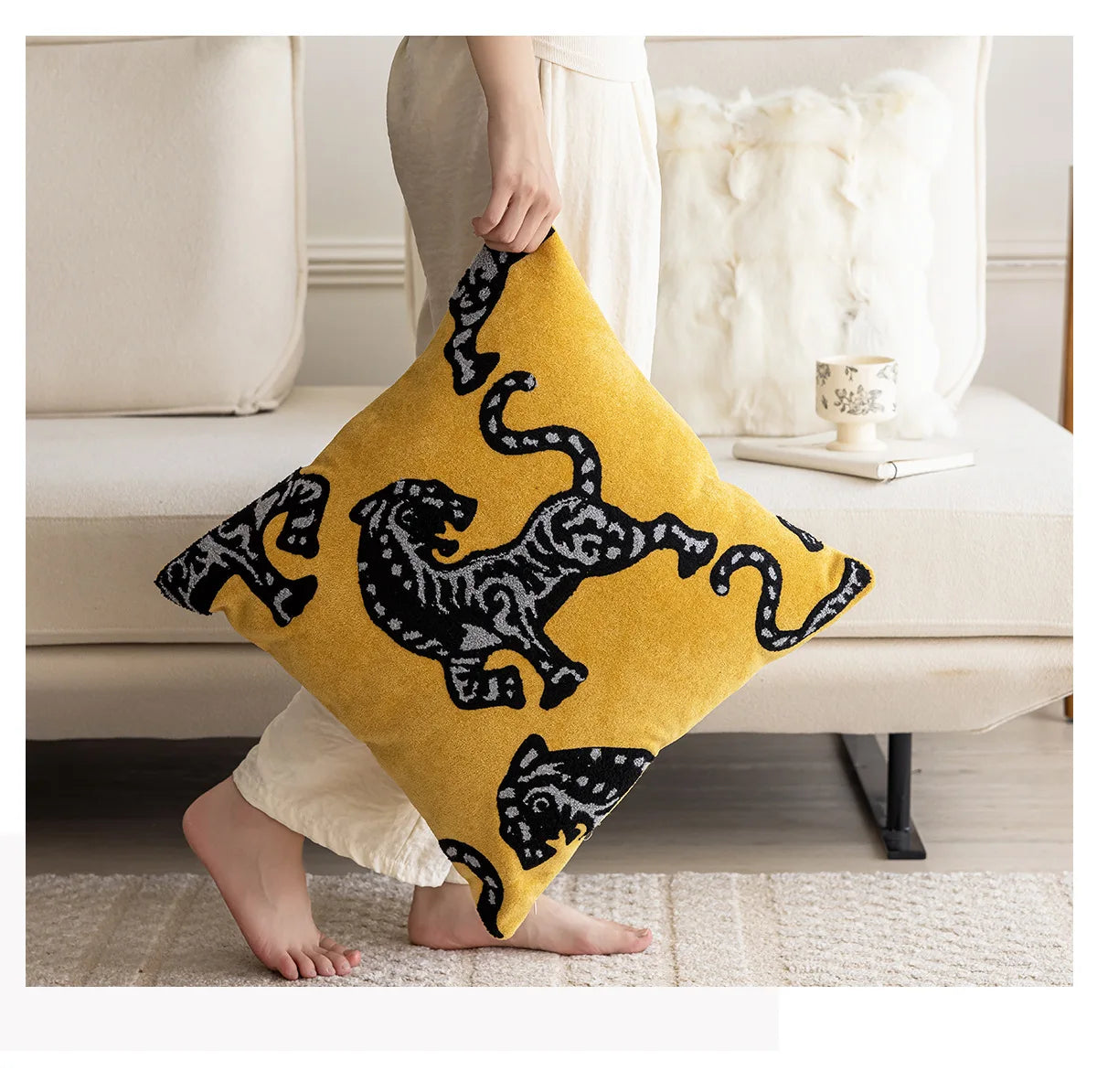 Person holding a yellow pillow with black tiger design in a living room setting. Modern minimalist embroidered pillow cover for living room decor