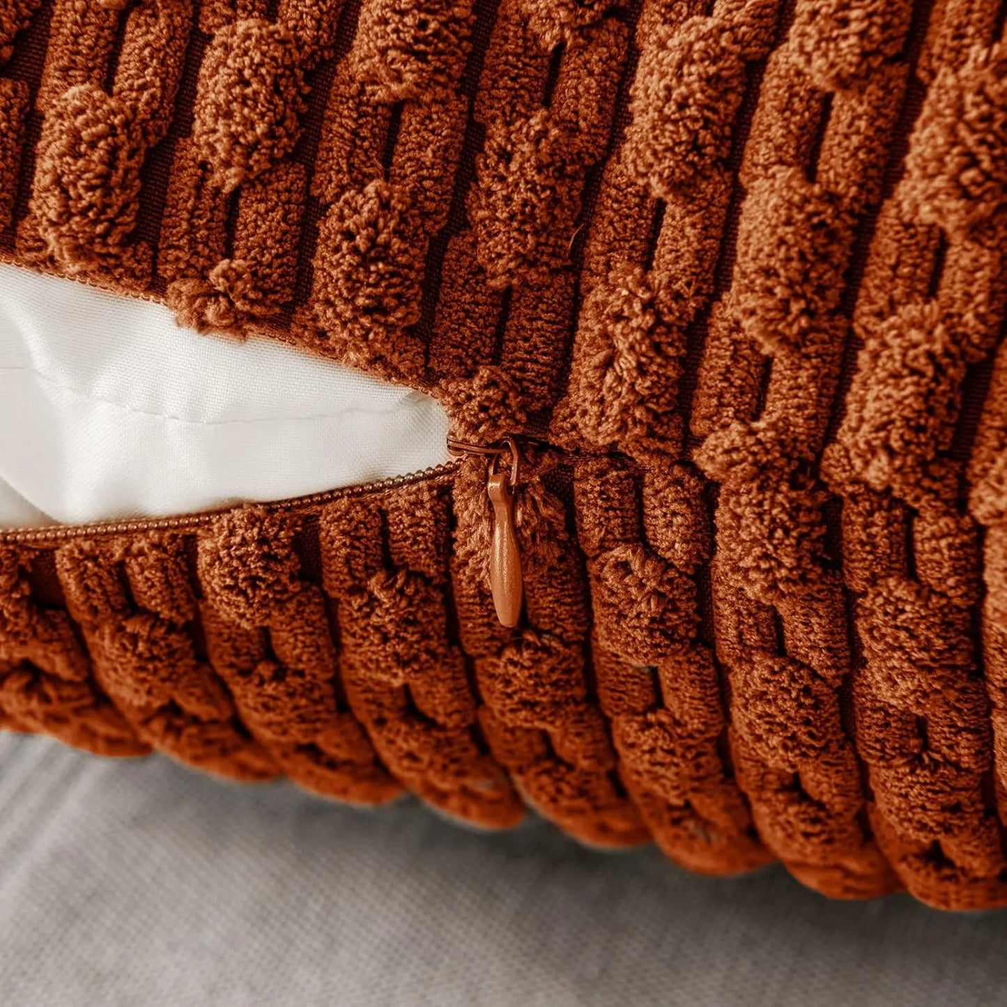 Close-up of a brown orange rust textured pillow with a zipper on a light gray background