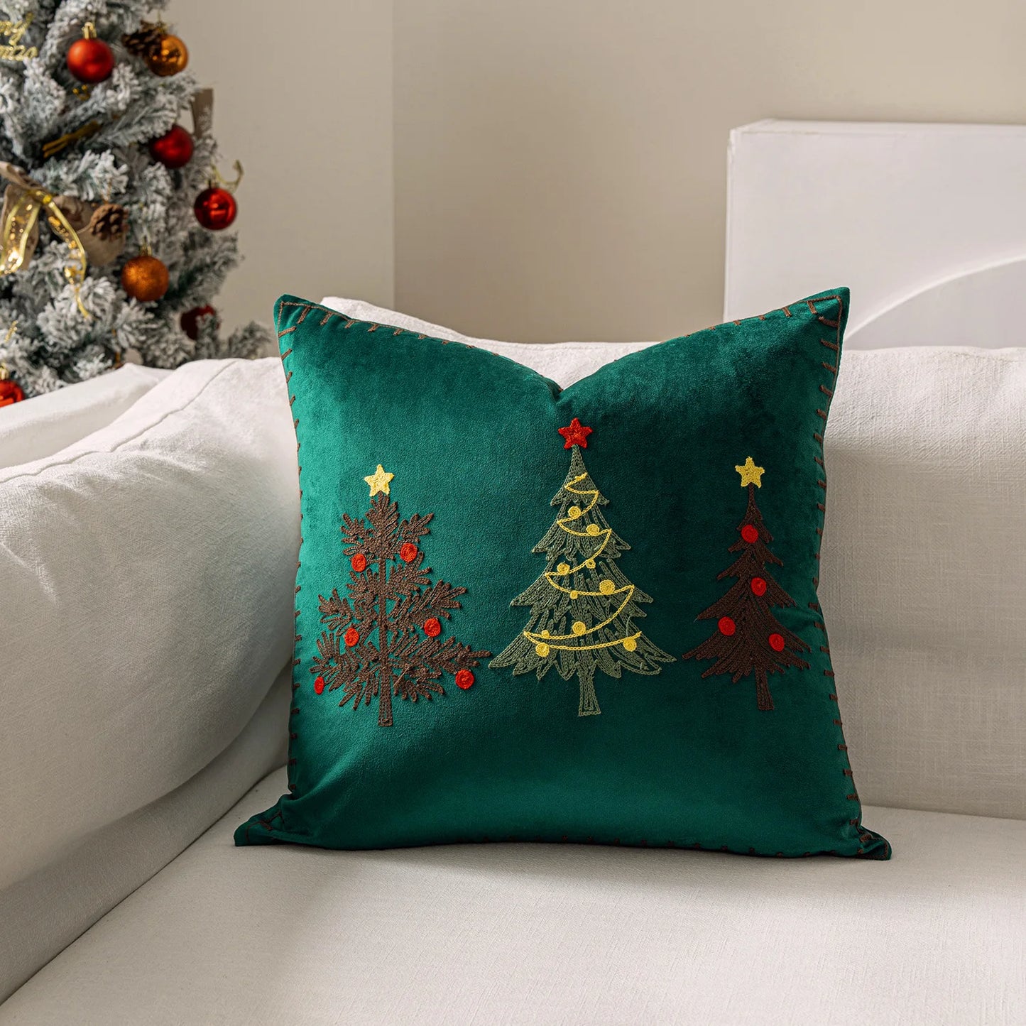 Green pillow with embroidered Christmas trees on a white couch next to a decorated Christmas tree.