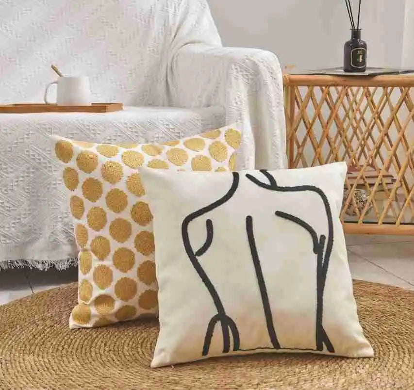 Two decorative pillows on a rug with a white chair and wooden side table in the background.