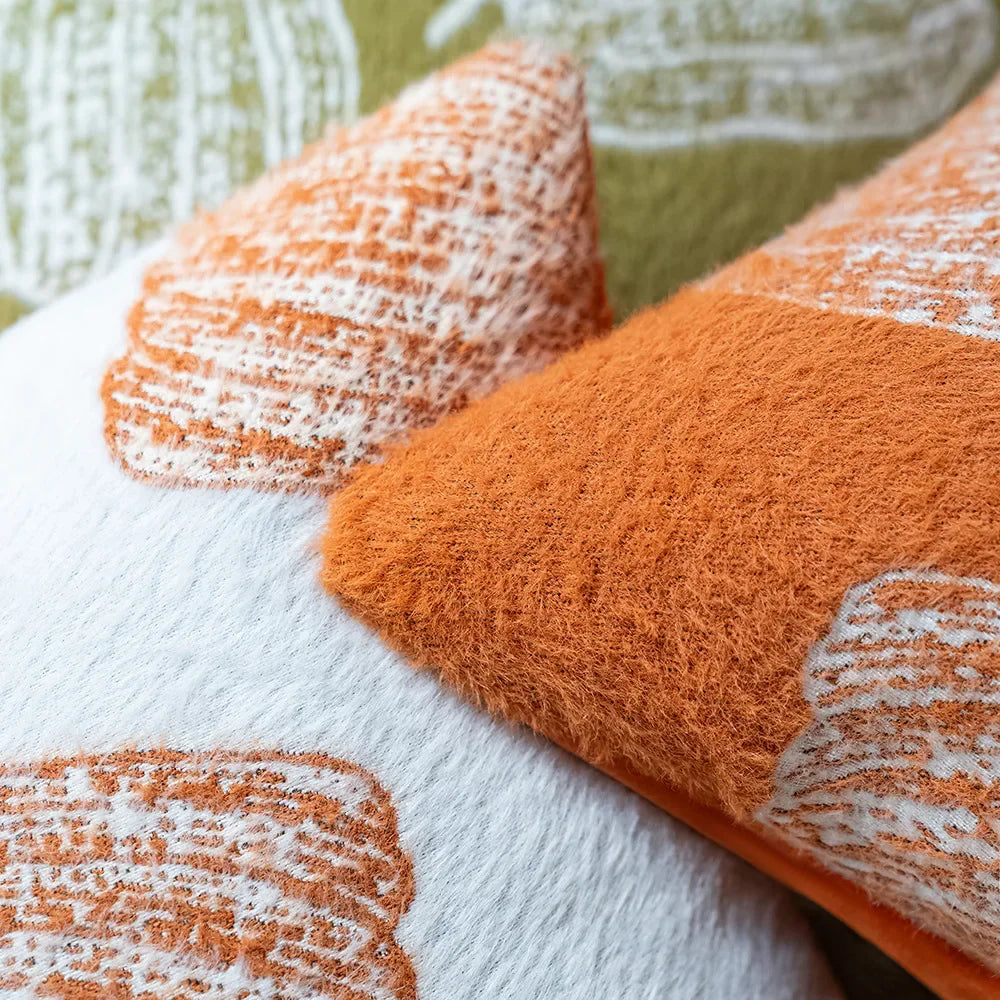 Close-up of orange and white textured fabric on a white surface with a blurred green background. Cozy fall pumpkin pillow cover for living room or bedroom.