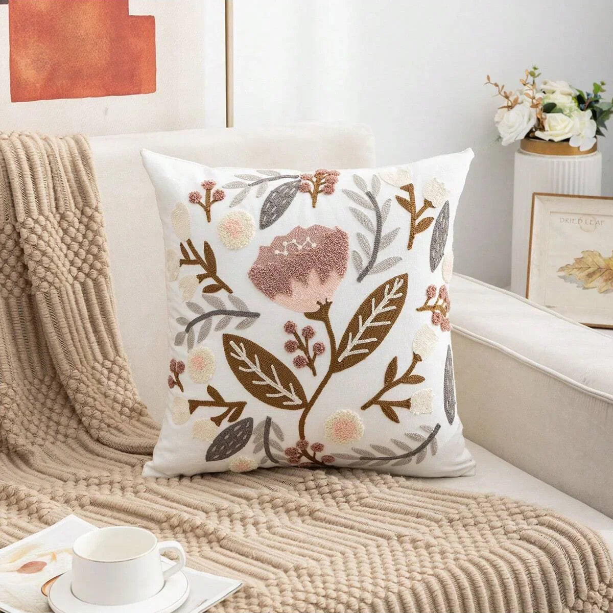 Decorative pillow with floral pattern on a couch with a blanket and cup. Embroidered flower pillow cover, 17.7-inch square canvas cushion case with floral design for sofa, bed, and boho home decor