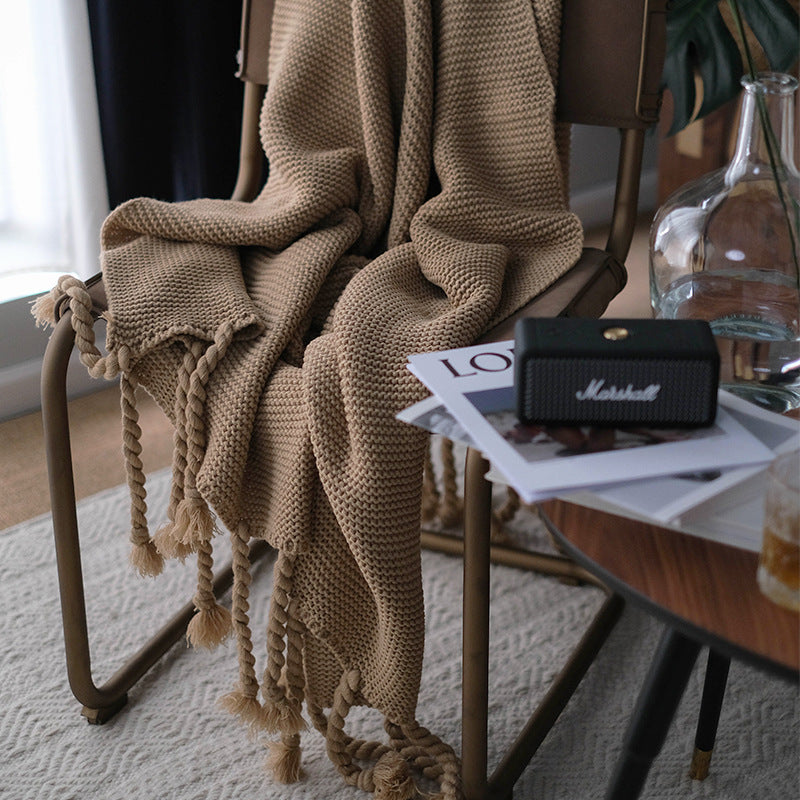 Brown knitted blanket draped over a chair with a Marshall speaker and magazine on a table in the background.
