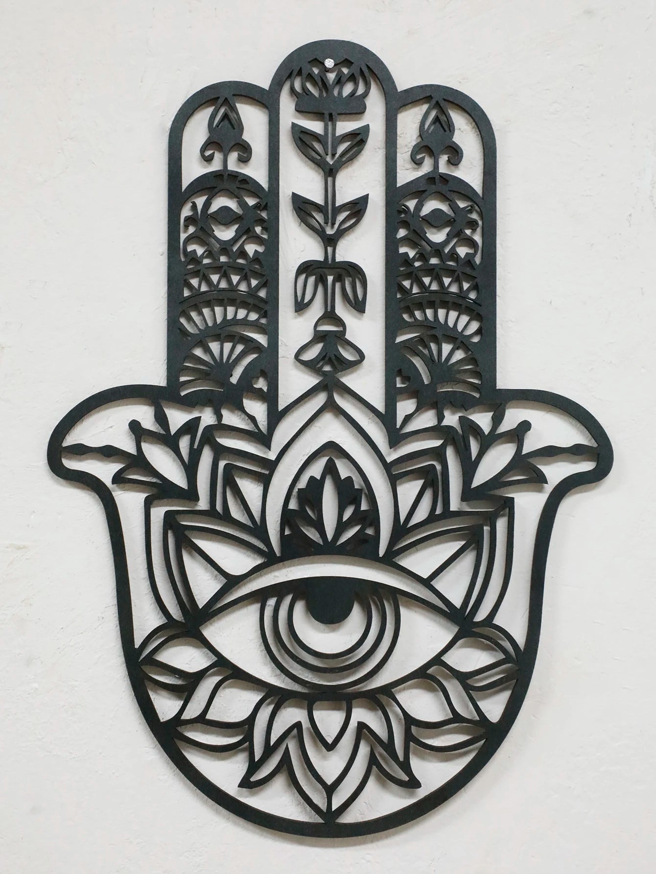 Black hamsa hand-shaped wood wall decor with protective evil eye, photographed against neutral background for alternative boho room styling.