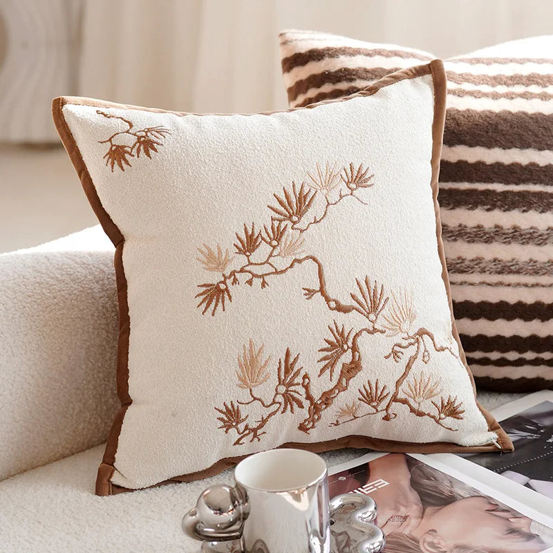 Decorative pillow with embroidered design on a couch with a striped pillow in the background. Nordic lily embroidered throw pillow cover in flannel fabric, floral square cushion case for sofa, bed, and boho home decor