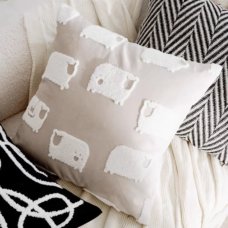 Decorative pillow with white embroidered sheep patterns on a neutral background