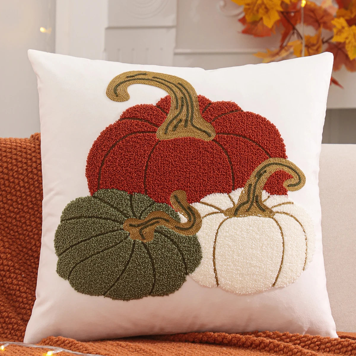 Decorative pillow with pumpkins on a couch. Velvet pillow cover with embroidered pumpkins, sunflowers, and autumn leaves – cozy fall home décor for sofa or living room.