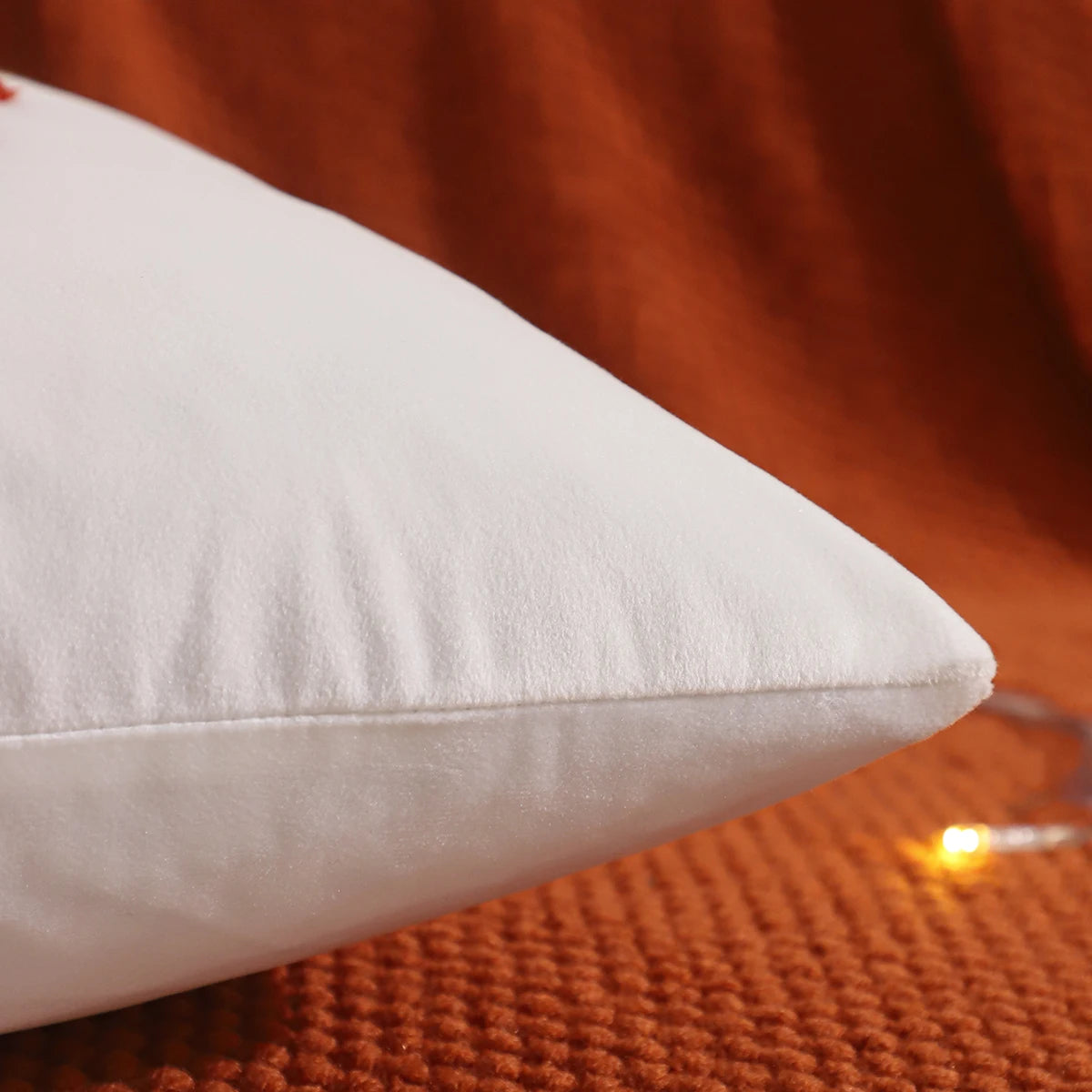 White pillow on a textured orange surface. Velvet pillow cover with embroidered pumpkins, sunflowers, and autumn leaves – cozy fall home décor for sofa or living room.