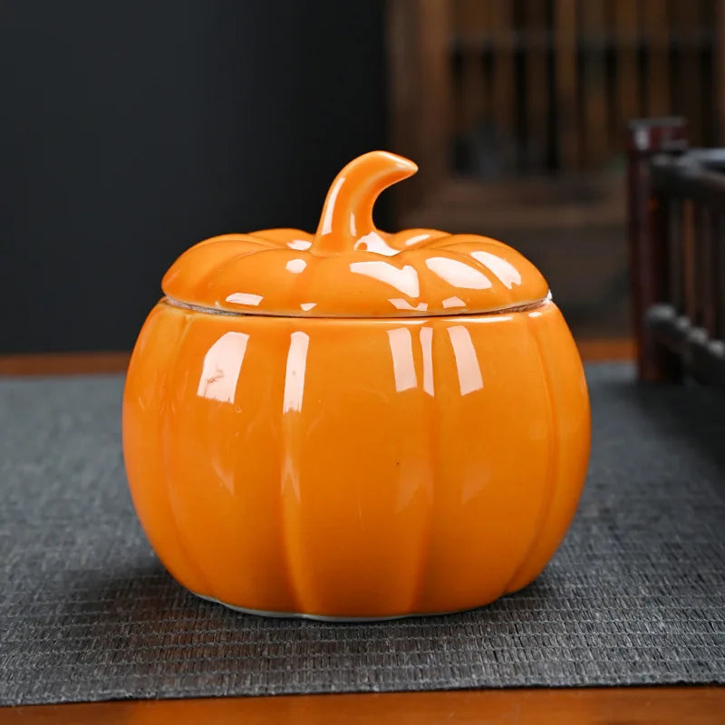 Orange pumpkin-shaped container with a lid on a dark surface. Ceramic pumpkin candy jar with lid, decorative fall tea jar or wedding gift container for home or halloween holiday decor.