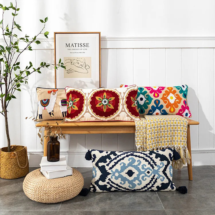 Colorful patterned pillows on a wooden bench with a plant and framed art in the background. Bohemian embroidered throw pillow cover with geometric design, cotton-blend cushion for sofa, bed, or modern home decor.