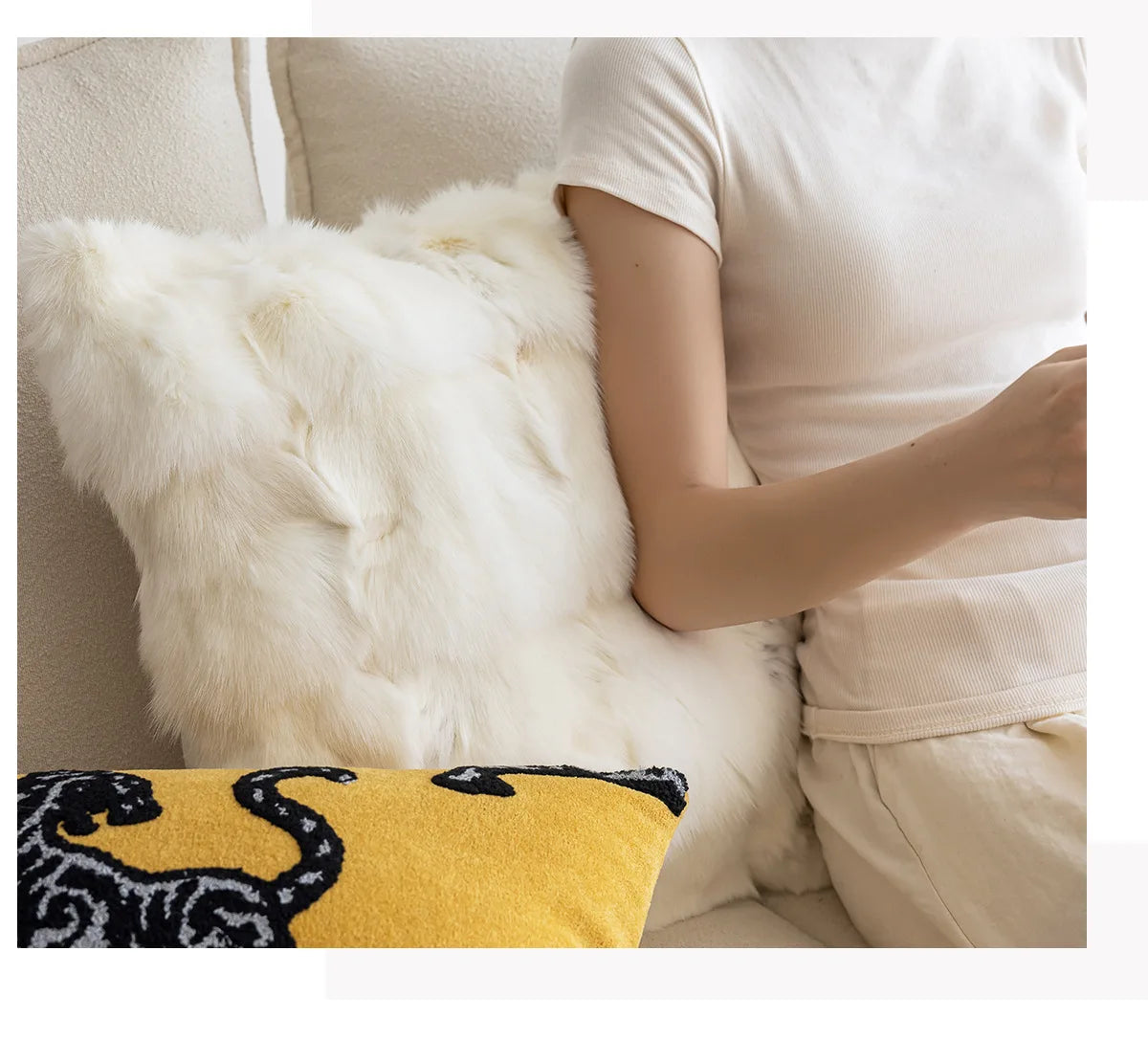 Person sitting on a couch with a white fur throw and a yellow pillow with a black design. embroidery throw pillow cover in boho modern style.