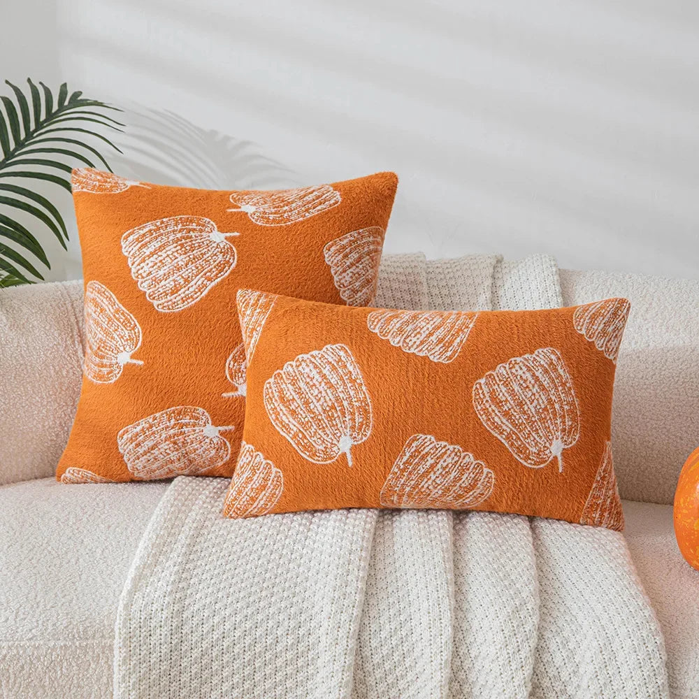 Two orange pillows with white patterns on a beige couch. Cozy fall pumpkin pillow cover for living room or bedroom.