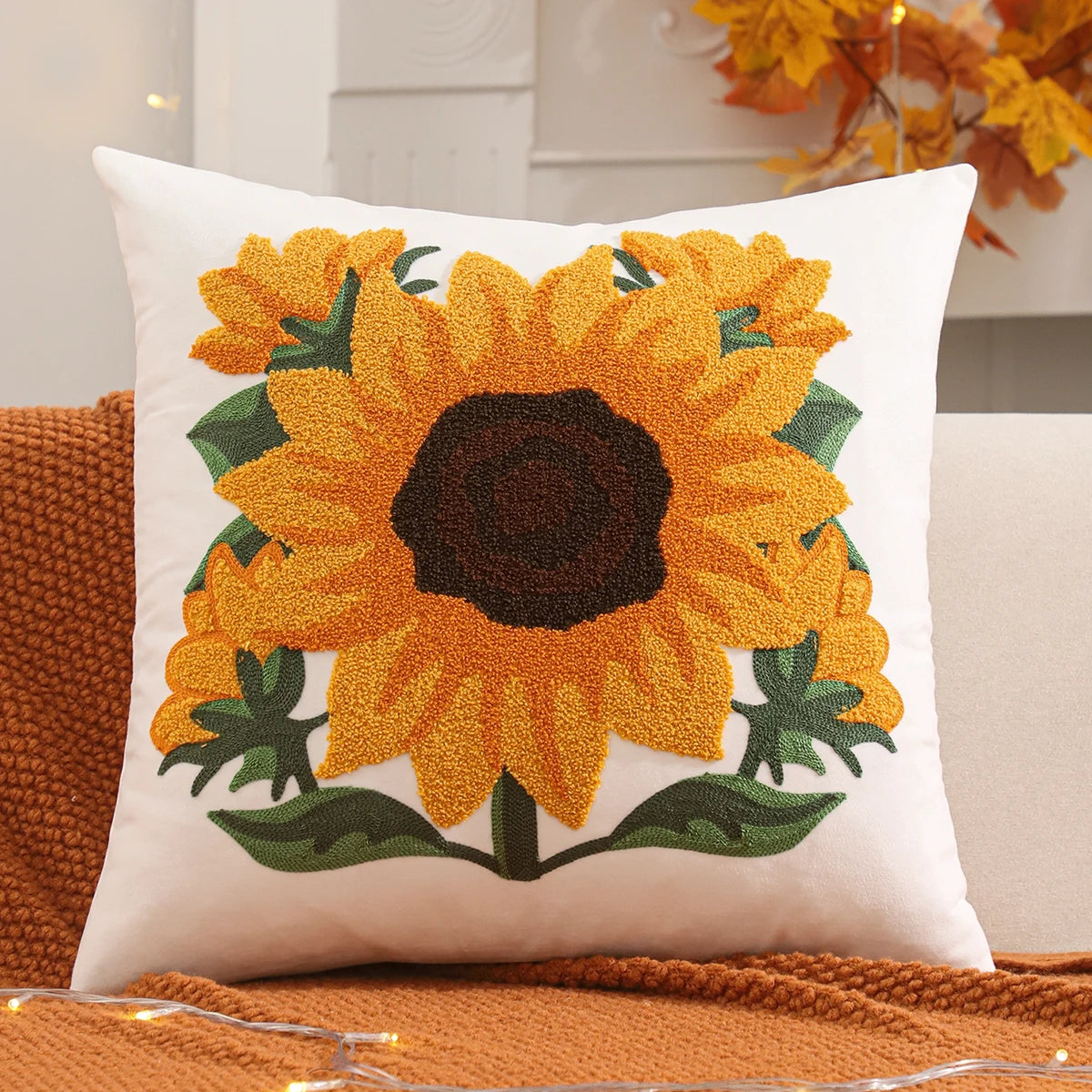 Decorative pillow with sunflower design on a couch. Velvet pillow cover with embroidered pumpkins, sunflowers, and autumn leaves – cozy fall home décor for sofa or living room.