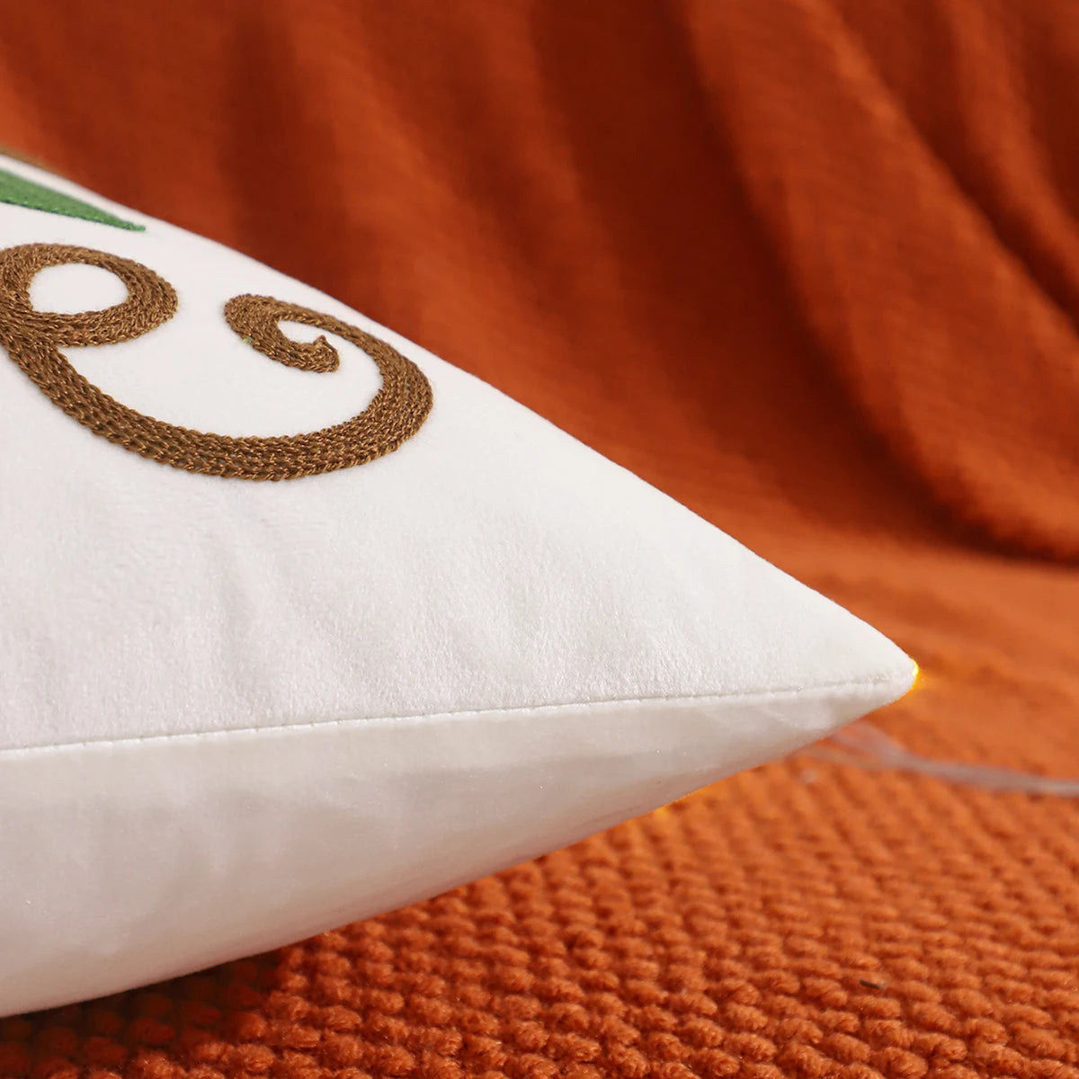 White pillow with embroidered design on an orange textured surface. Velvet pillow cover with embroidered pumpkins, sunflowers, and autumn leaves – cozy fall home décor for sofa or living room.