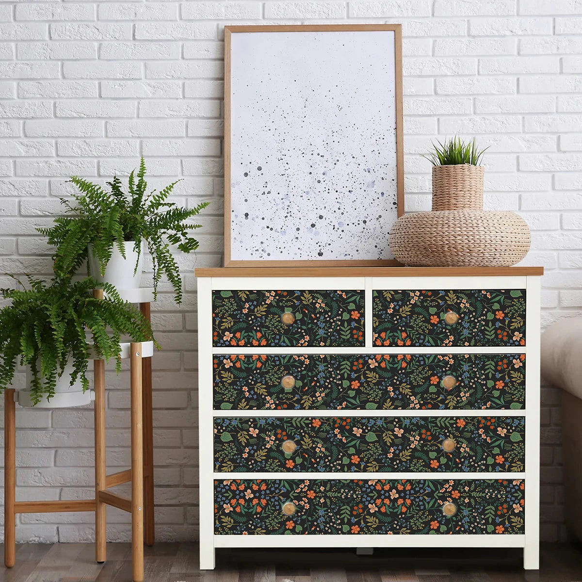 White dresser with floral patterned drawers against a white brick wall with plants and a framed picture. Black floral peel-and-stick wallpaper roll, 40 x 120 cm, waterproof and moisture-proof wall covering for stylish home decoration