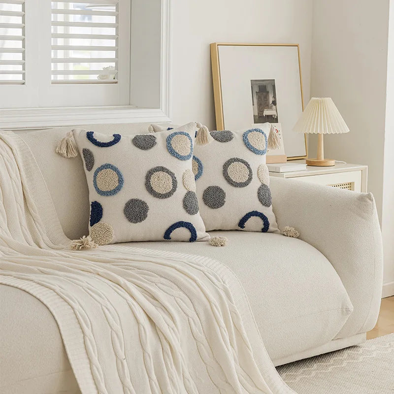 Decorative pillows with circular patterns on a beige sofa in a living room. Nordic blue tufted cushion cover with geometric stripe and grid crochet pattern, tassel pillow cover for sofa, bed, and boho home decor