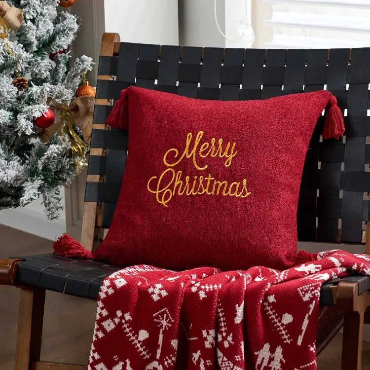 Red pillow with 'Merry Christmas' text on a black woven bench next to a decorated Christmas tree.