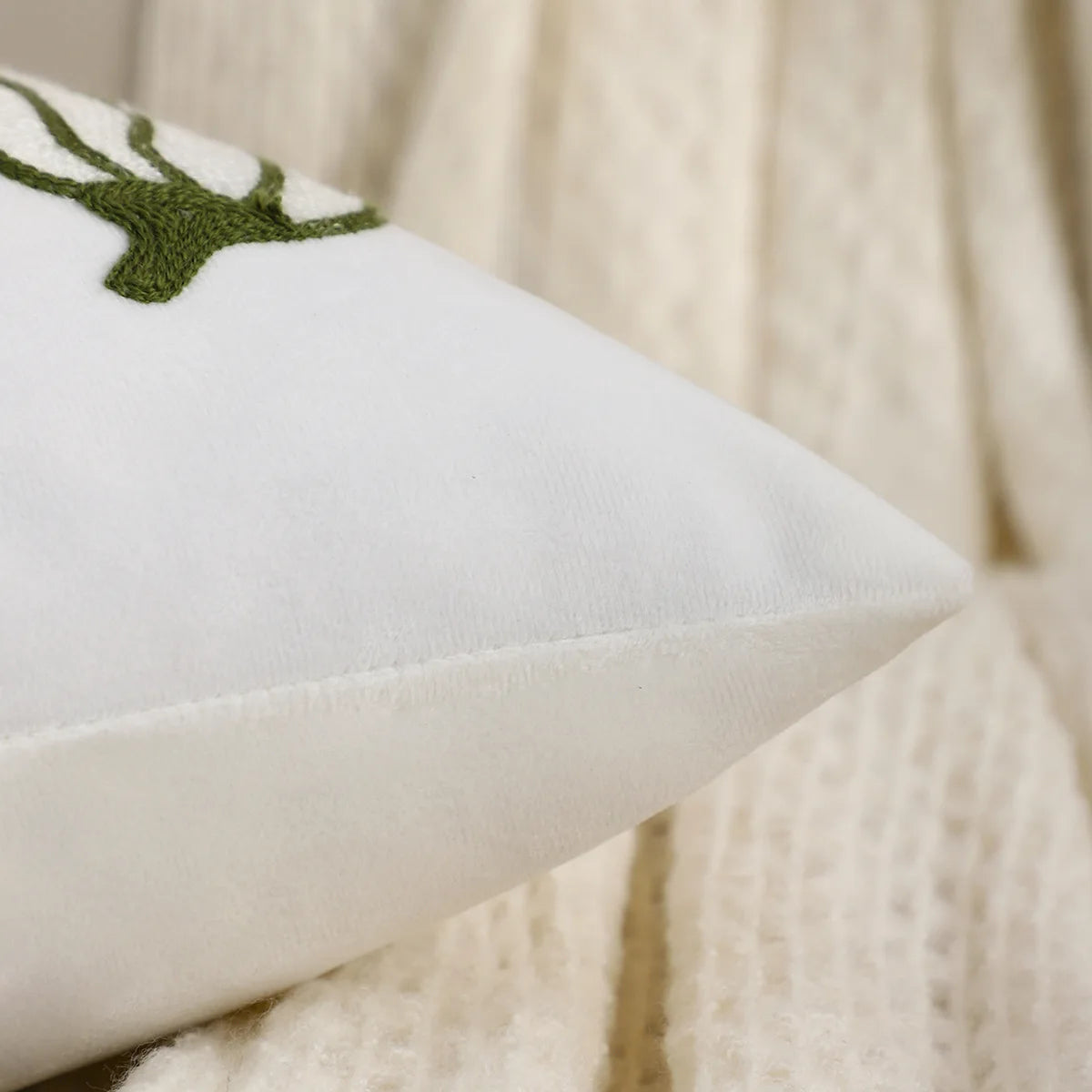 White pillow with green embroidered design on a beige background