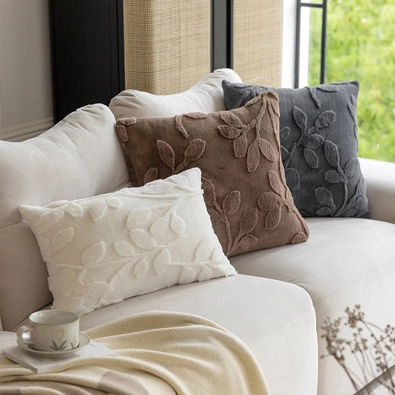 Decorative pillows on a sofa with a cup and blanket in a cozy living room. Modern jacquard leaf throw pillow cover, woven floral decorative cushion for sofa, bed, or living room in neutral and soft tones.
