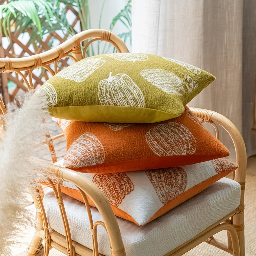 Stack of colorful pillows on a wicker chair with a neutral background. Cozy fall pumpkin pillow cover for living room or bedroom.