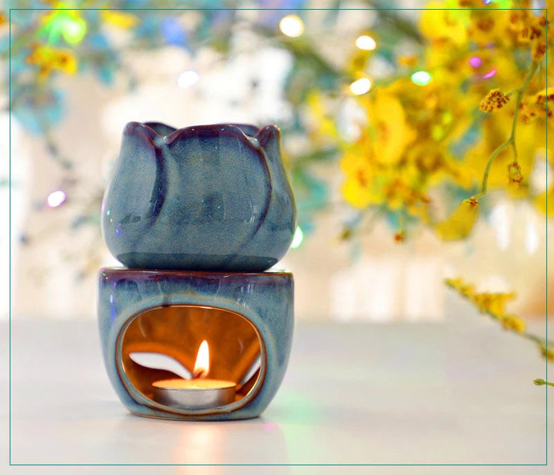 Blue ceramic oil burner with a lit candle inside, set against a blurred floral background. tulip ceramic essential oil incense burner, candle-powered aroma diffuser for home fragrance and calming boho home décor
