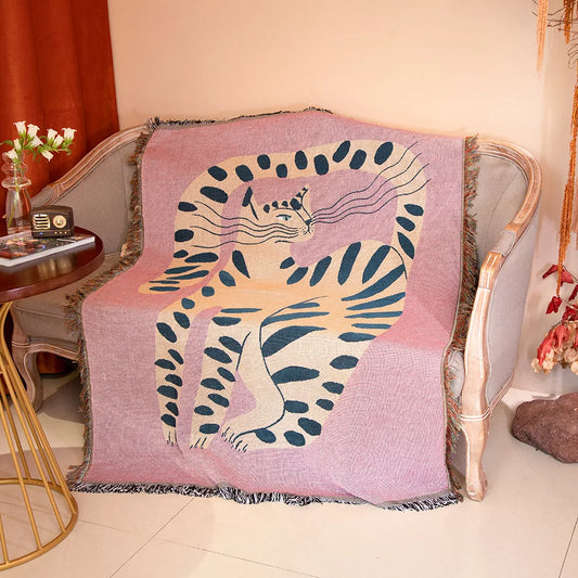Decorative blanket with a cat design draped over a chair in a cozy room. Pink cat cartoon throw blanket boho cotton sofa cover