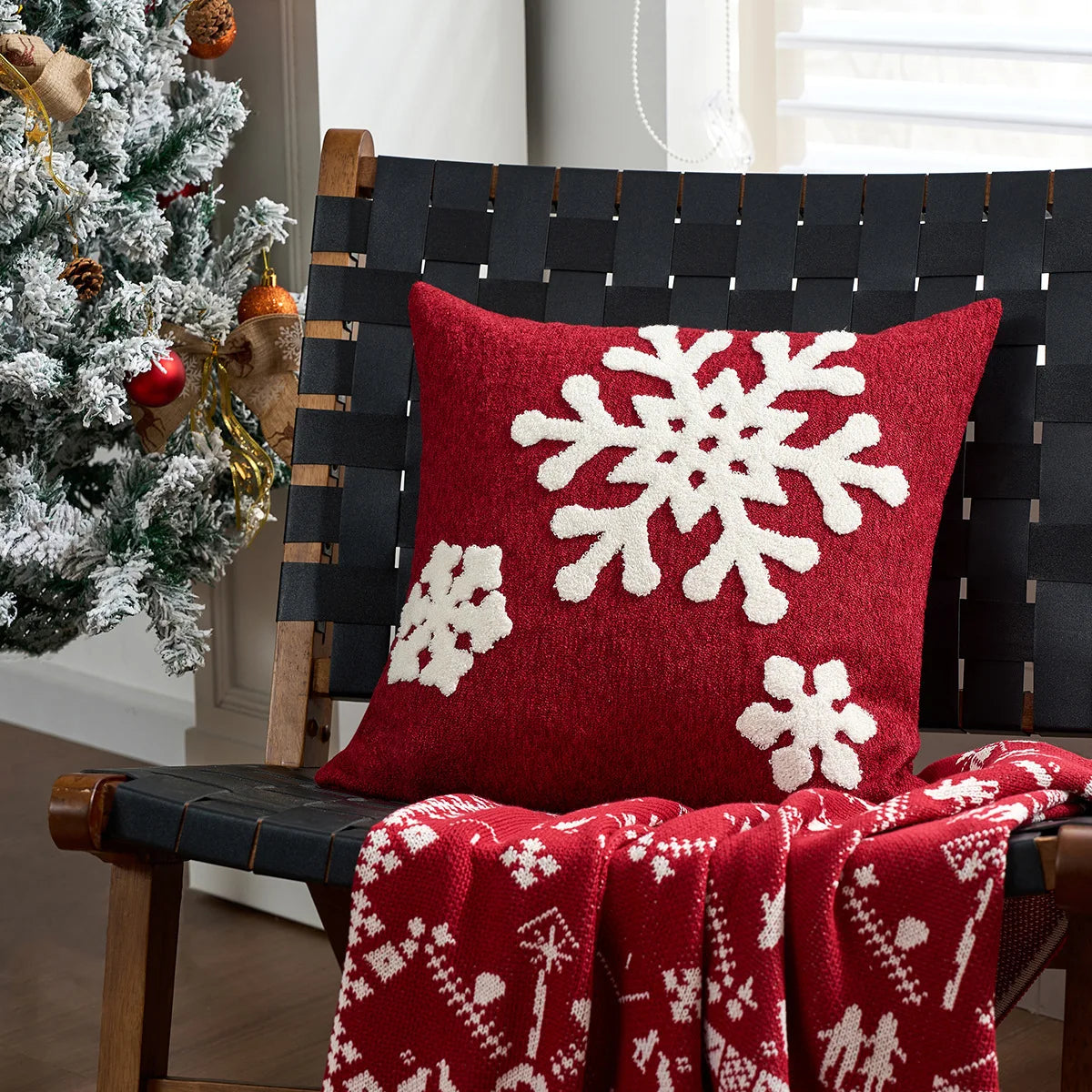 Red pillow with white snowflake patterns on a black woven chair next to a decorated Christmas tree.
