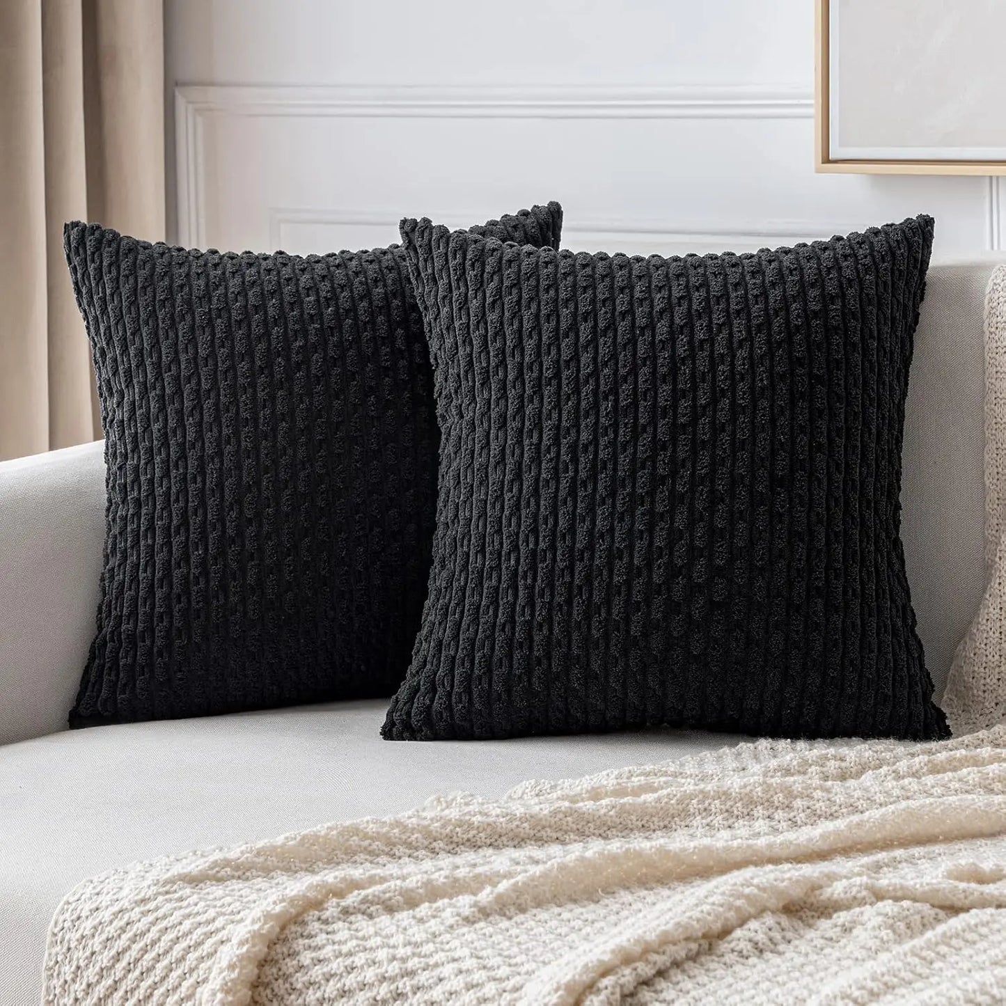 Two dark gray black textured pillows on a light-colored sofa with a beige blanket.