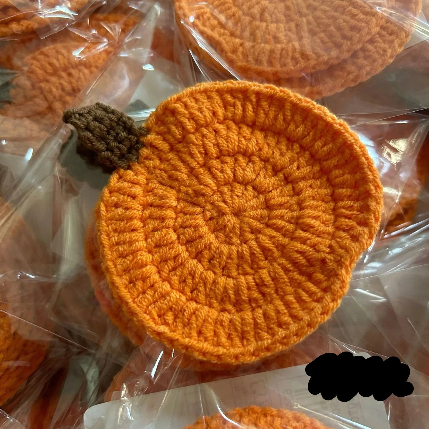 Crocheted orange coasters with a central button on a clear plastic background. Handmade crochet pumpkin coaster in cotton, Halloween table decor for mugs and drinks, festive DIY autumn party accessory