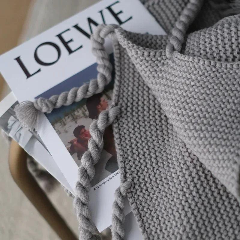 Gray knitted blanket with tassels on a magazine featuring LOEWE branding.