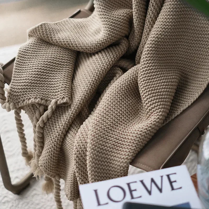 Beige knitted blanket draped over a chair with a LOEWE sign in the foreground.