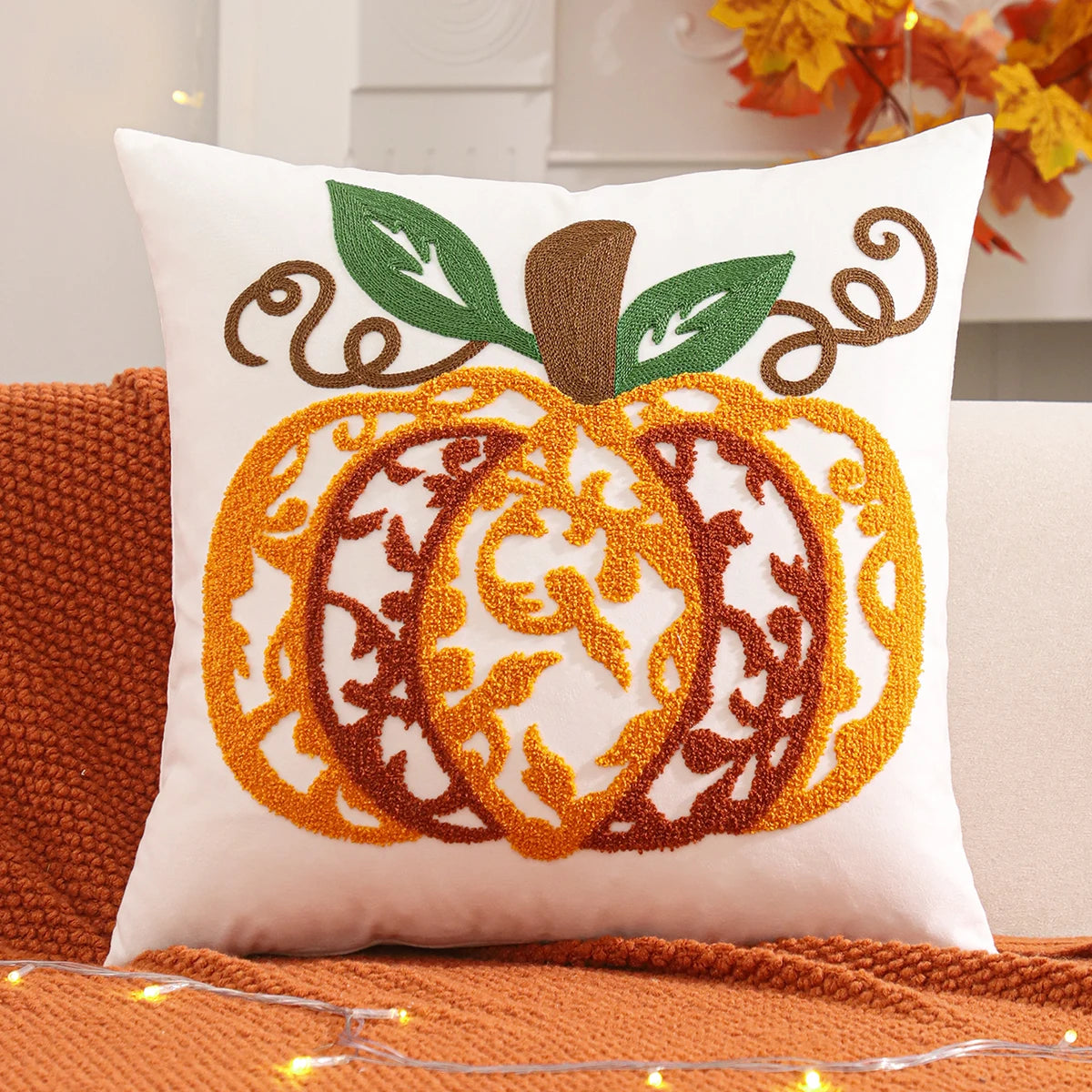 Decorative pillow with pumpkin design on an orange couch. Velvet pillow cover with embroidered pumpkins, sunflowers, and autumn leaves – cozy fall home décor for sofa or living room.