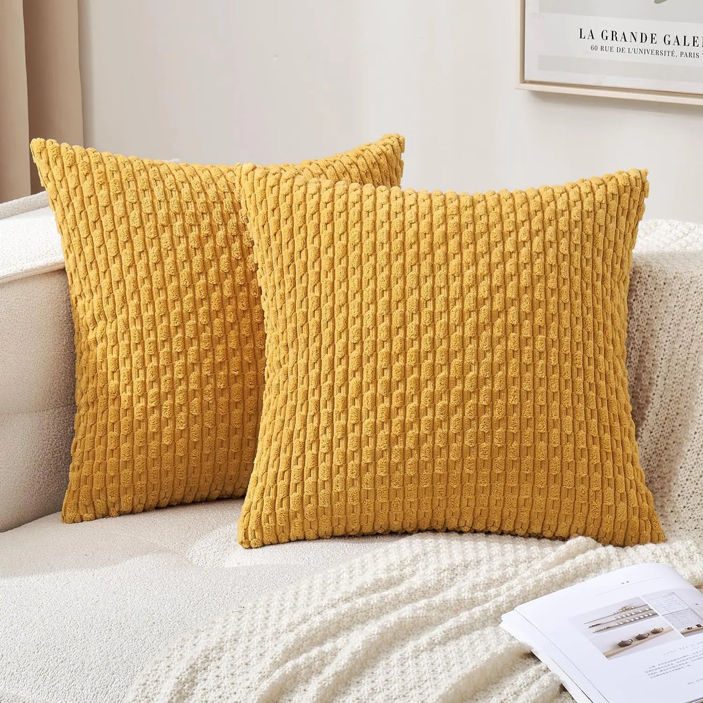Two textured yellow pillows on a beige sofa with a white blanket and magazine.