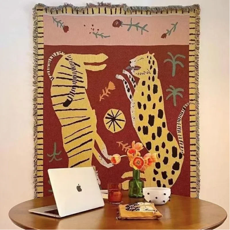 Decorative blanket with animal design on a table with a laptop and other items. Two leopard tapestry throw blanket, boho woven cotton blend blanket for sofa or bed