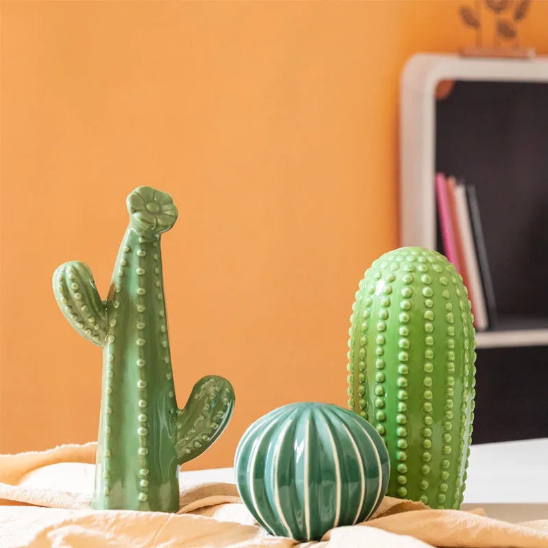Three green cactus-shaped objects on a surface with an orange wall in the background. Boho Nordic cactus decor prop for photography and interiors
