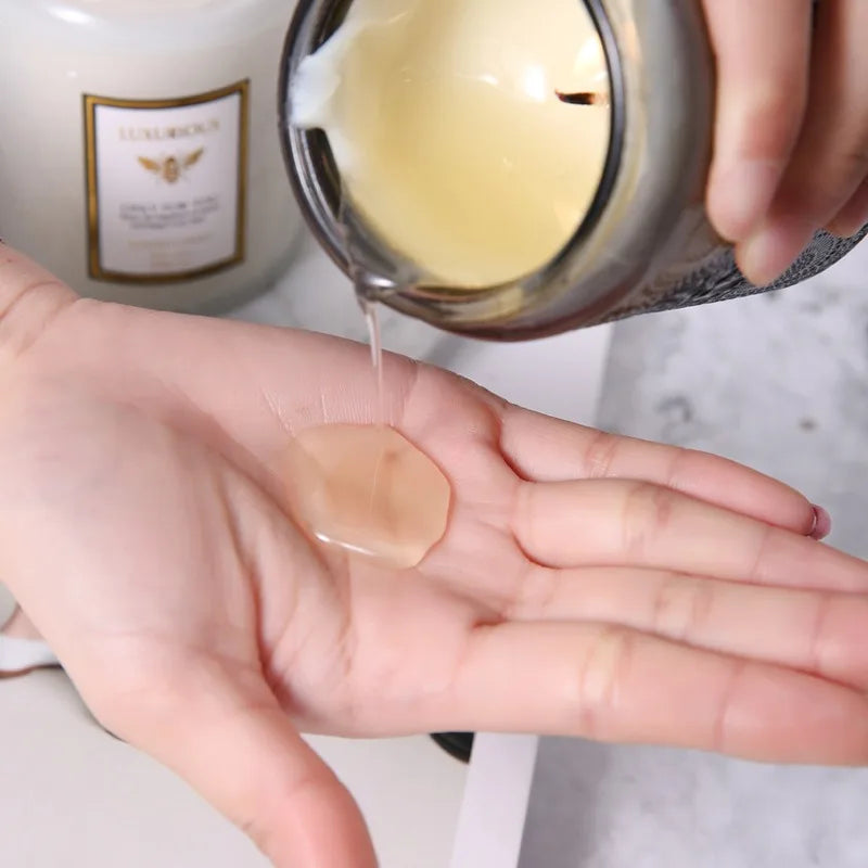 Hand pouring melted soy wax from a container onto another hand with a blurred background.