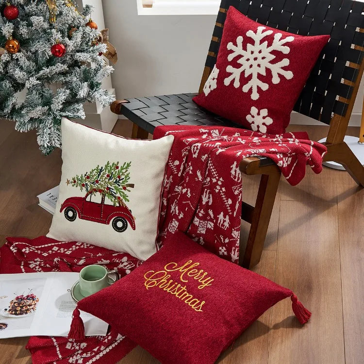Decorative pillows with Christmas designs on a chair next to a tree. Christmas gold letter embroidered pillow cover with “Holly Jolly” and snowflake design, soft red and white chenille cushion case for sofa or living room holiday décor.