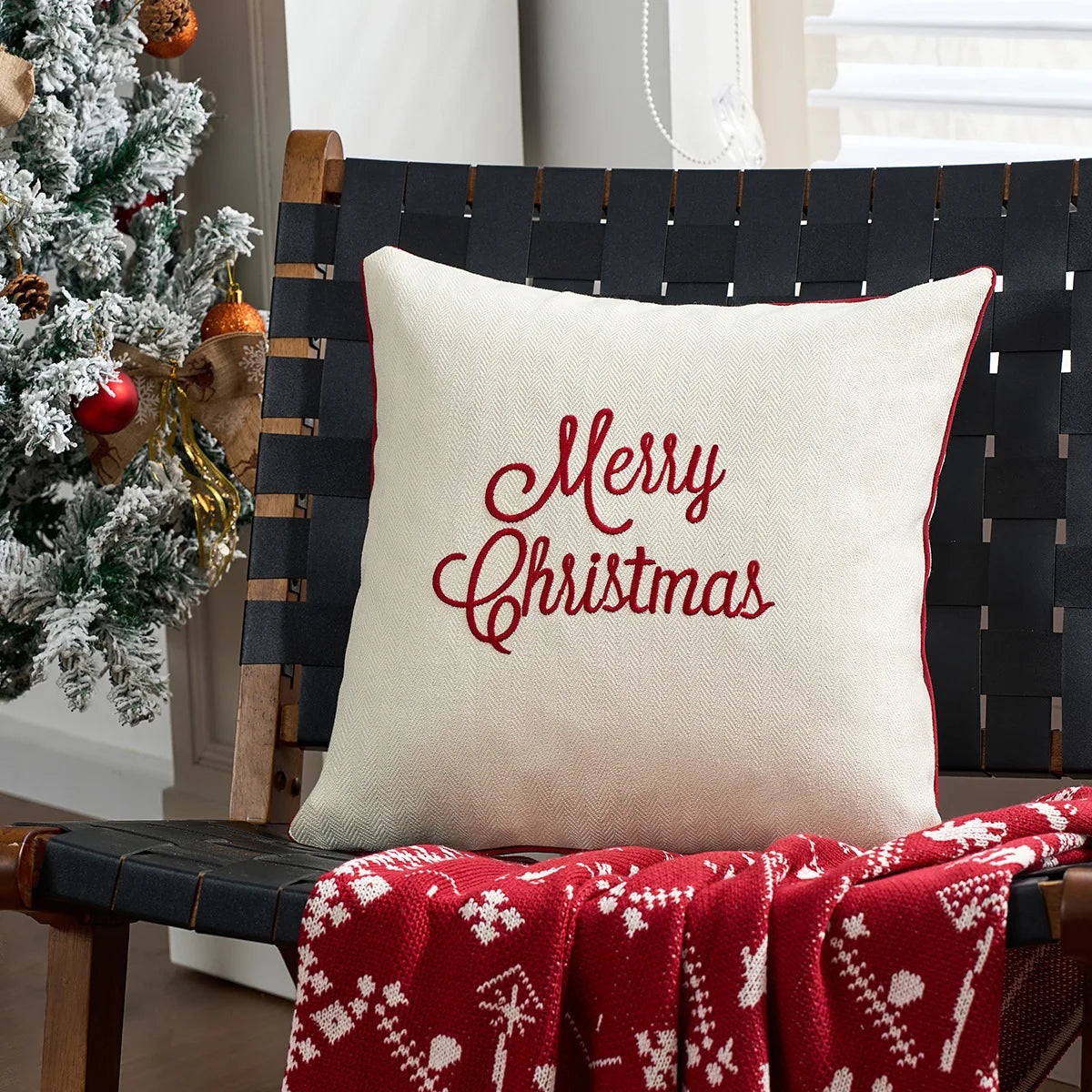 Decorative pillow with 'Merry Christmas' text on a chair next to a Christmas tree.