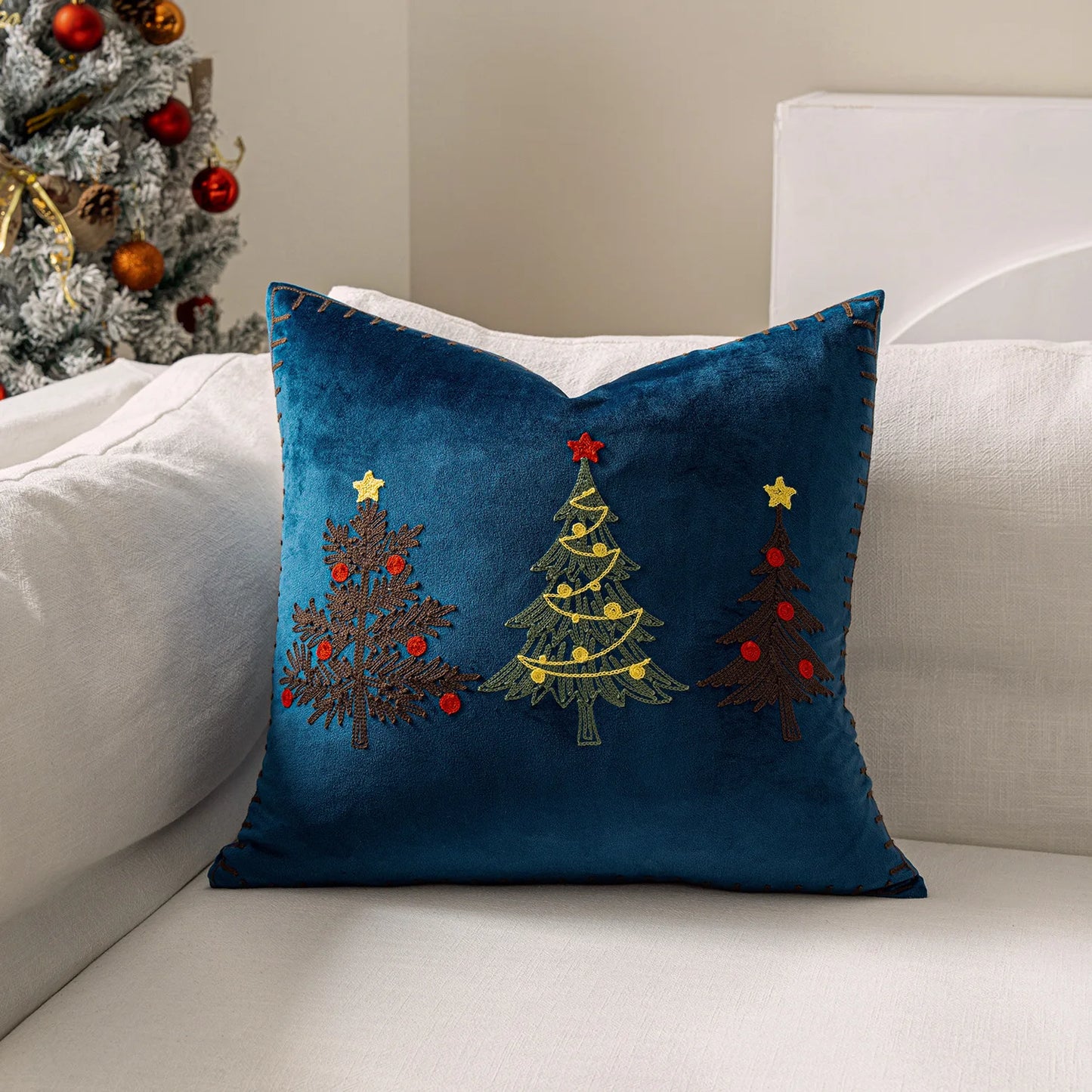 Blue pillow with embroidered Christmas trees on a white couch